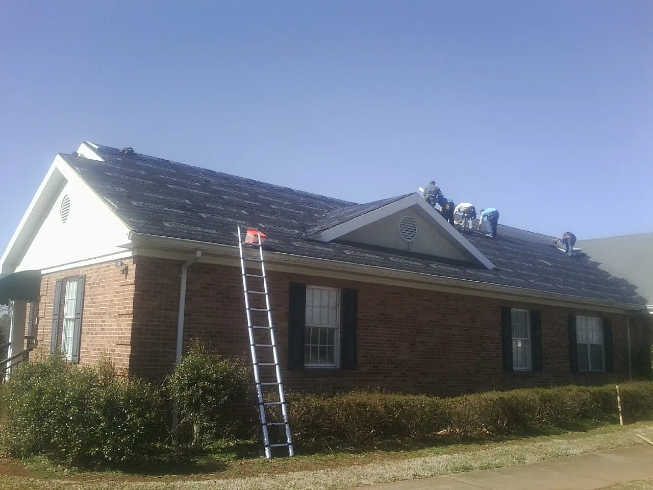 Crew tearing shingles off a brick ranch roof with a ladder set — Metal Roof Repair work by our crew in Browns Mills