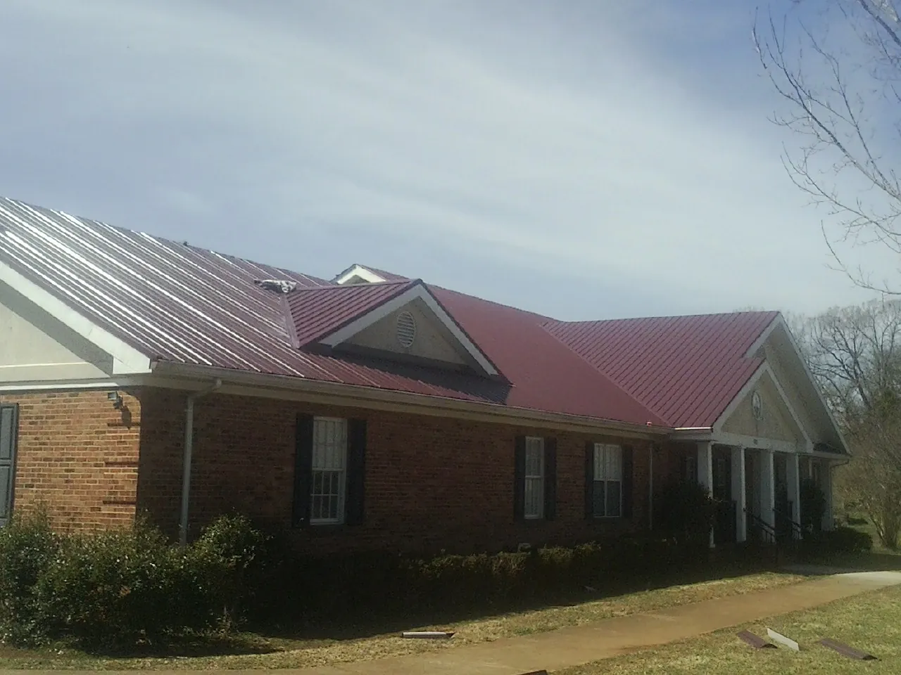 Red metal roof with gabled entries on a long brick building, from a Hail Damage Roof Repair job in Browns Mills