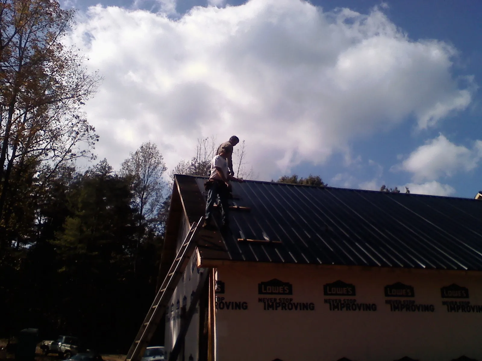 Roofer fastening dark metal panels high against a cloudy sky, from a Roof Inspection job in Browns Mills