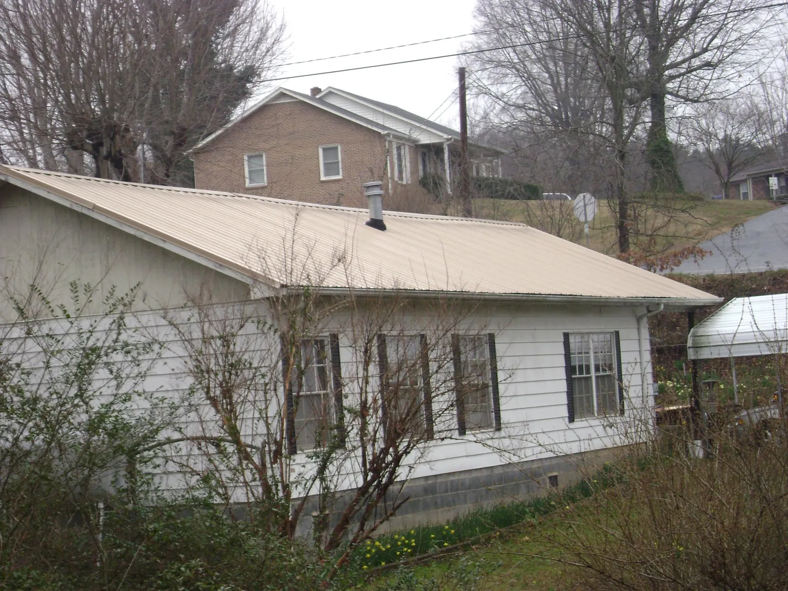 Tan metal roof on a white sided house set into a hillside — Commercial Roofing by Roofing Brothers in Browns Mills